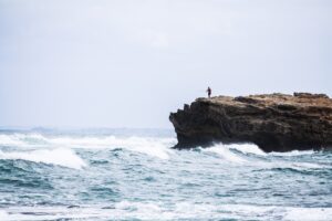 Solo human casts fishing line into sea from a rocky cliff