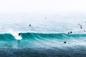 Surfers catching waves in a teal sea