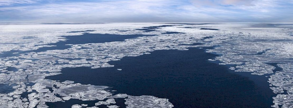 Image of a birds-eye view of the Arctic ocean basin. There is open water surrounded by chunky sea ice.