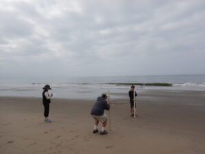 Image shows three people taking sand measurements at the beach